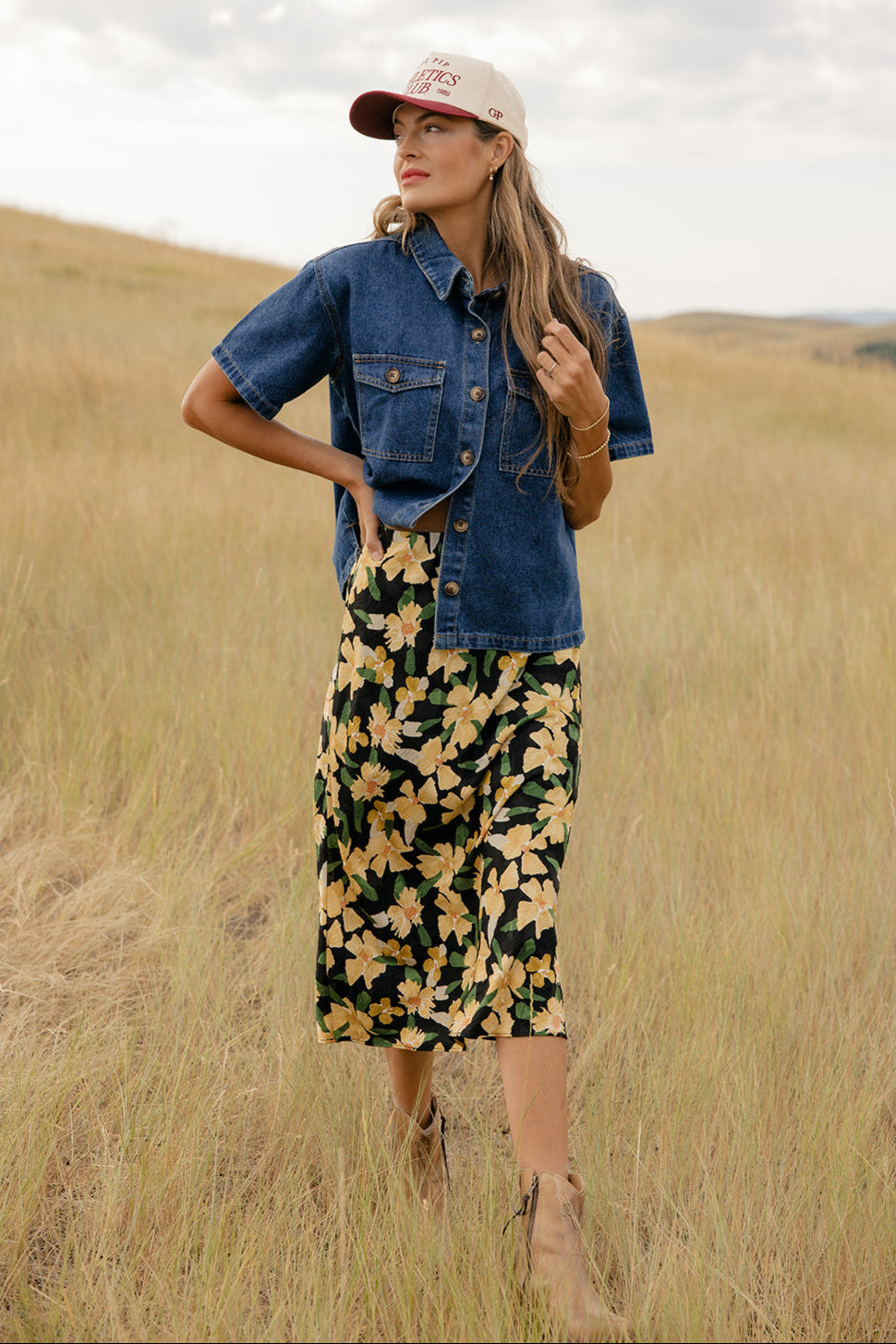 Woman in a denim jacket and floral dress standing in a field