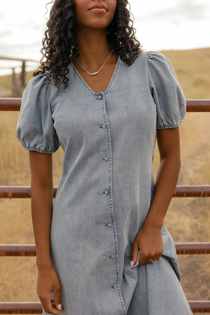Woman wearing a denim dress with puff sleeves in an outdoor setting