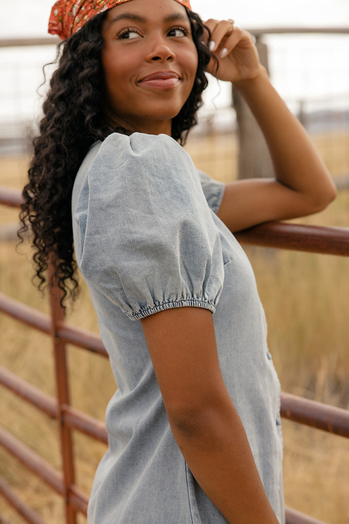 Woman wearing a light blue dress with short sleeves, standing outdoors.