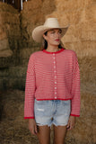 Woman wearing a red and white striped shirt and cowboy hat standing in front of hay bales.