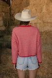 Person wearing a red and white striped shirt and a cowboy hat, standing in front of hay bales.