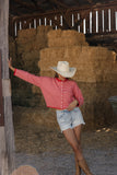 Person wearing a red and white striped shirt and white cowboy hat in a barn with hay bales.