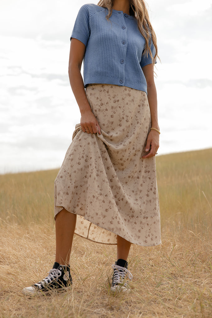 Person wearing a blue top and beige skirt with floral pattern in a field