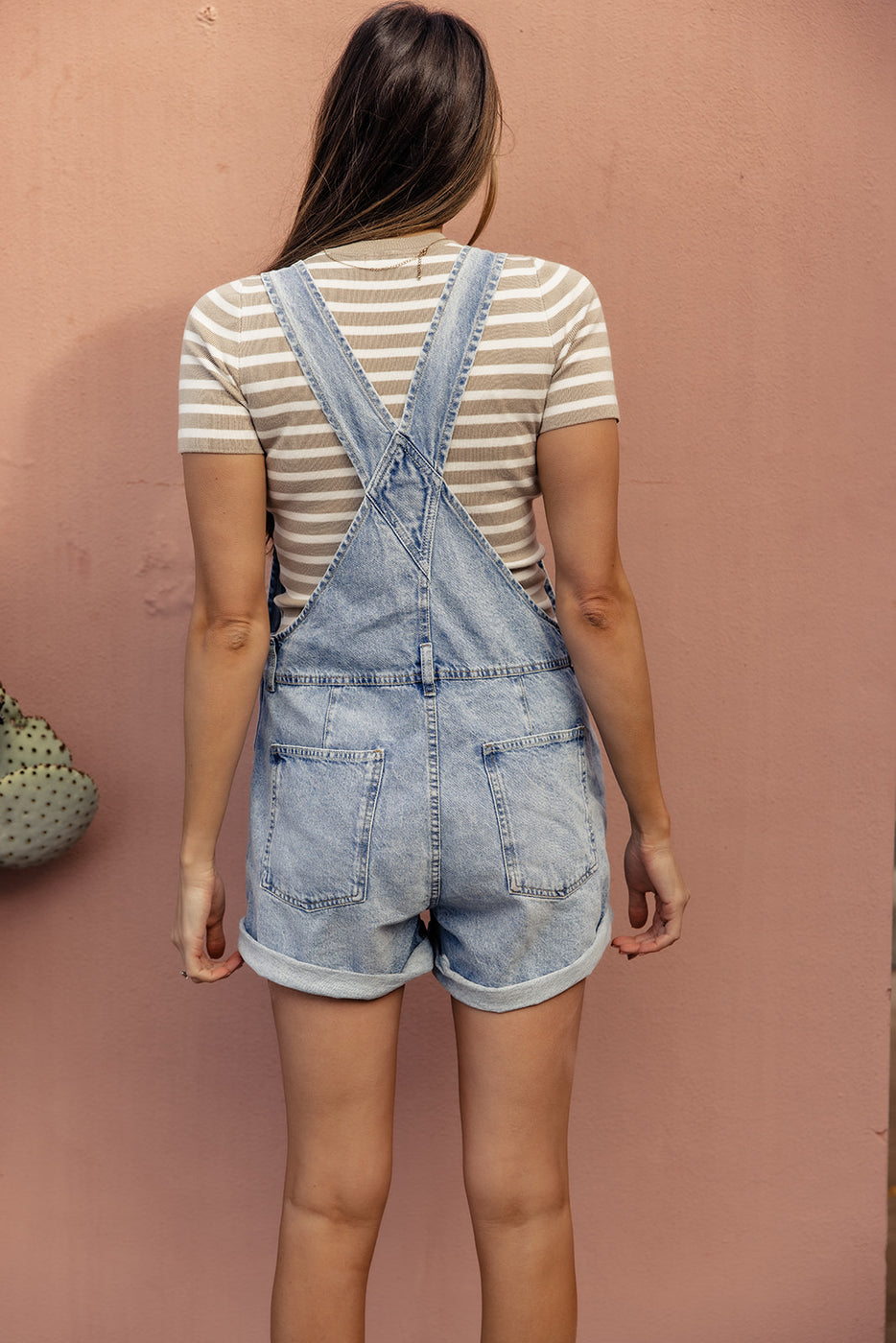 a woman in overalls standing in front of a pink wall