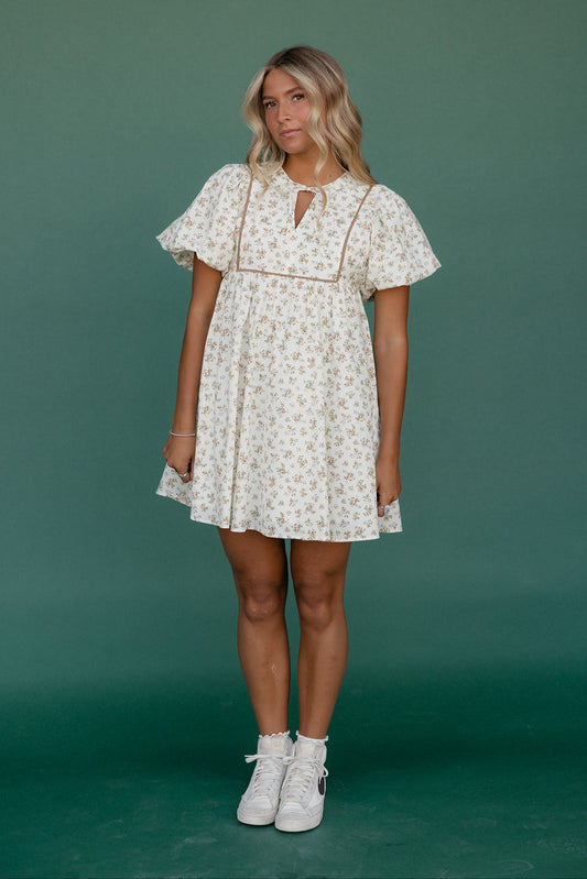 Woman wearing a floral dress with white sneakers against a green background