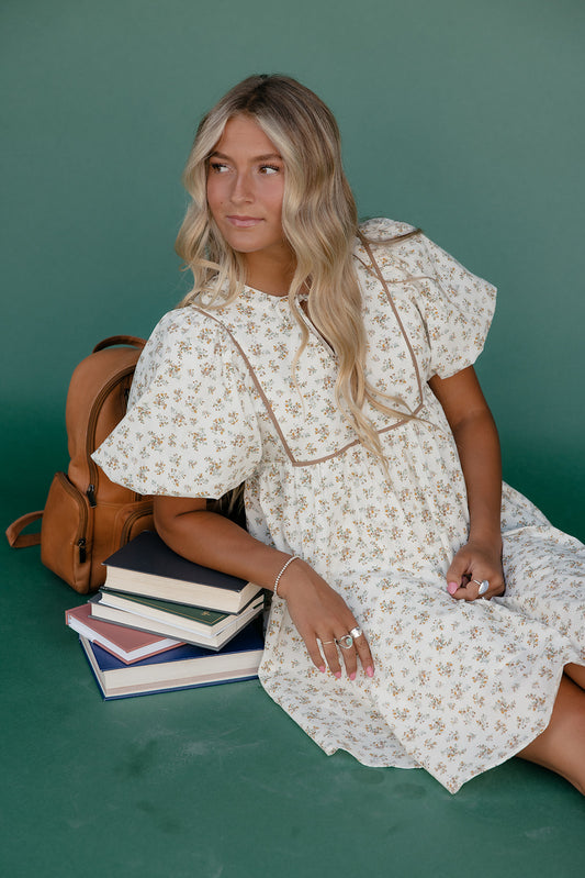 Woman in a floral dress sitting with books and a backpack on a green background