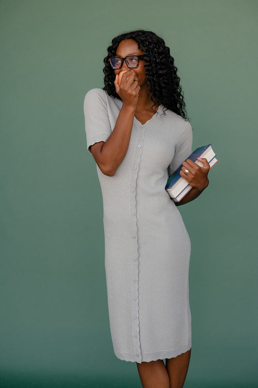 Woman in a gray dress holding books against a green background