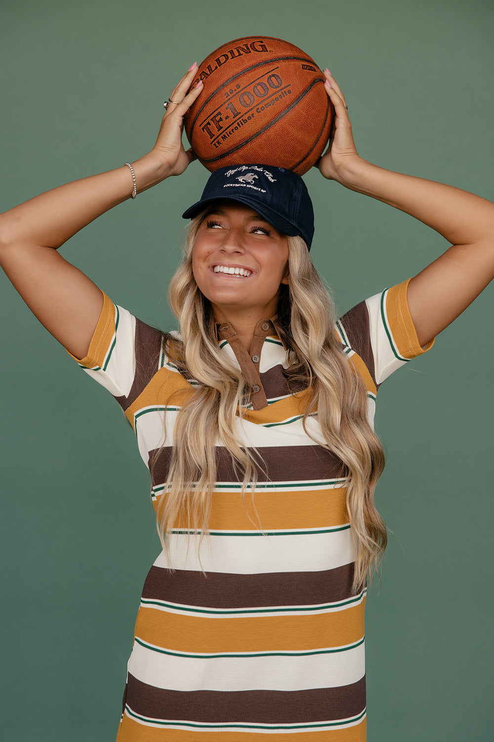 Woman holding a basketball above her head against a green background