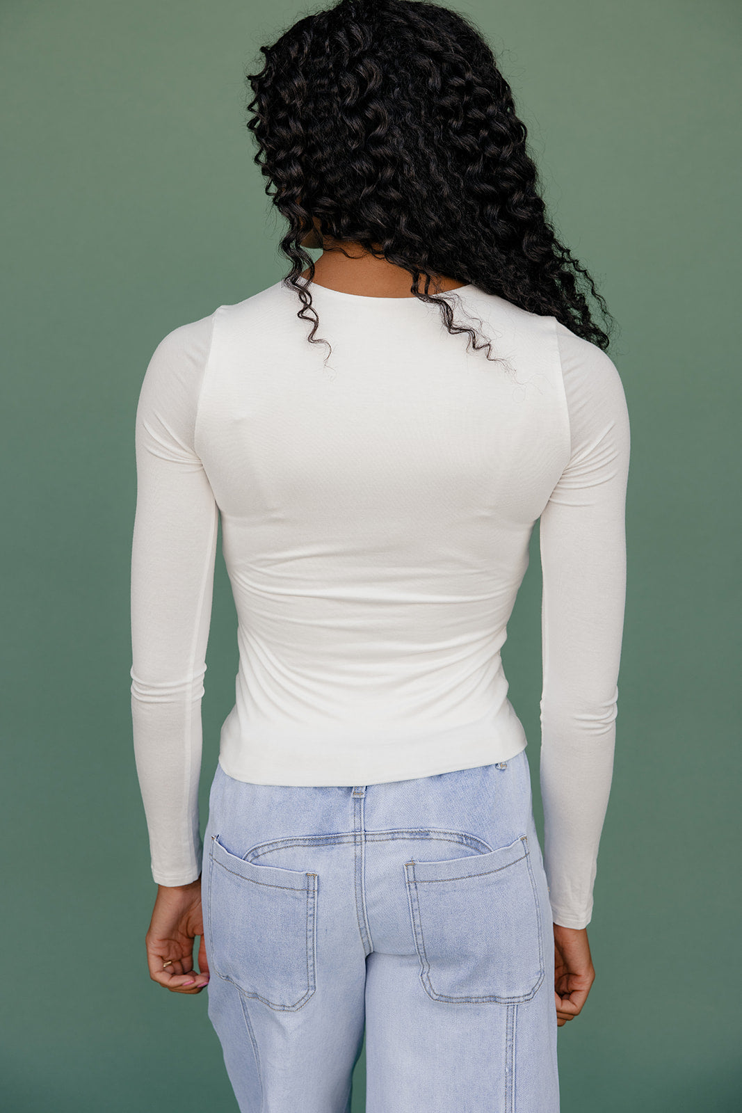 Person wearing a white long-sleeve top and light blue jeans against a green background