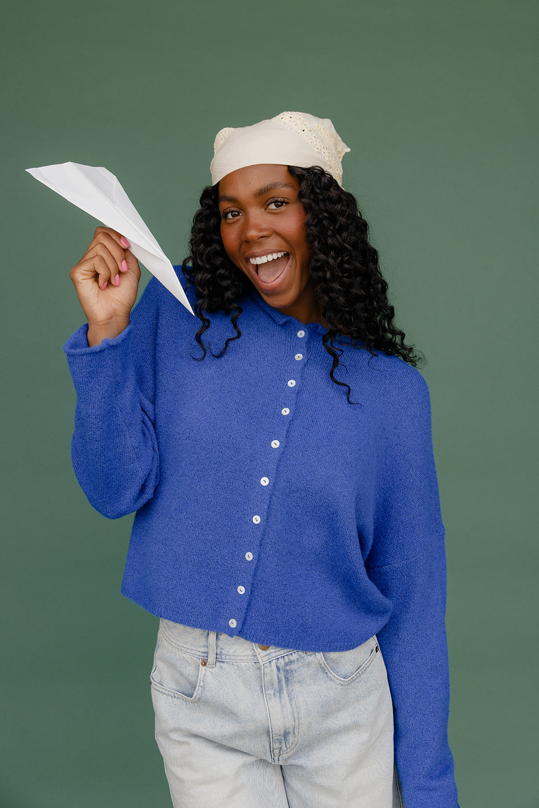 Person holding a paper airplane against a green background