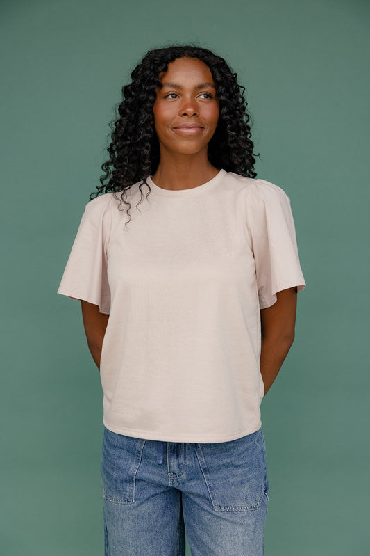 Woman wearing a beige t-shirt and blue jeans against a green background
