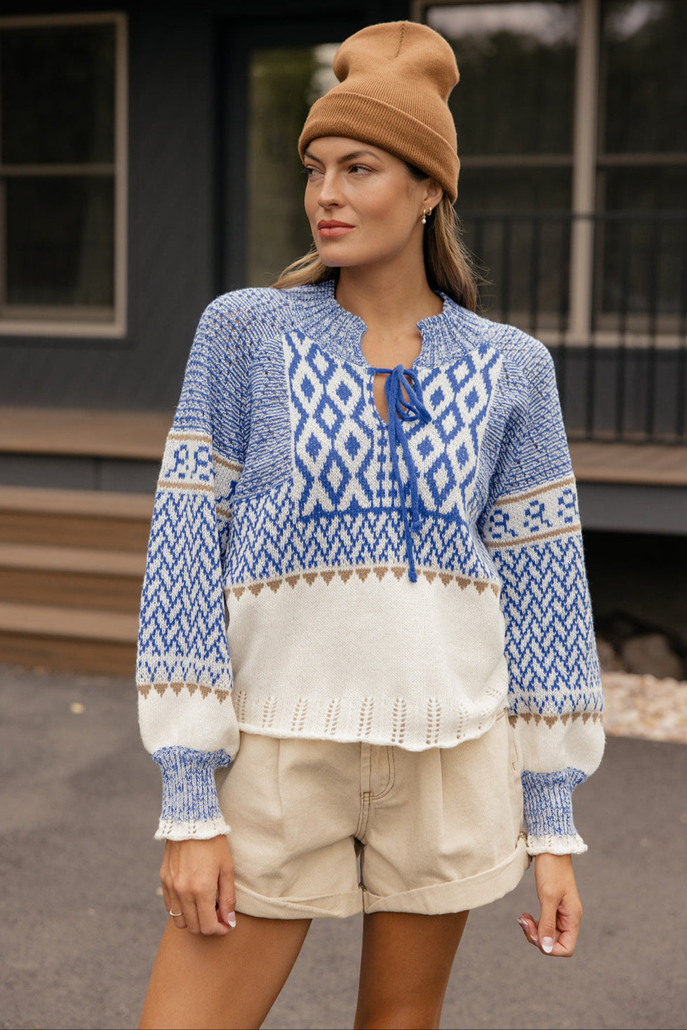 Woman wearing a blue patterned sweater and beige shorts outdoors.