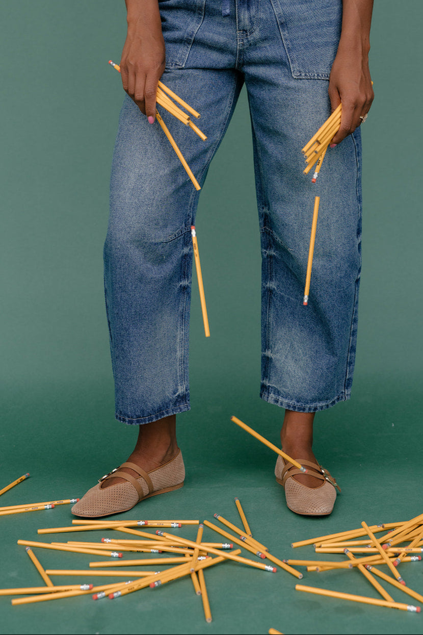 Person wearing blue jeans holding yellow pencils against a green background