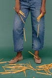 Person wearing blue jeans holding yellow pencils against a green background