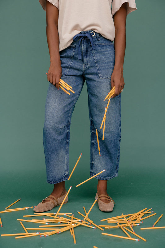 Person wearing blue jeans holding yellow pencils against a green background