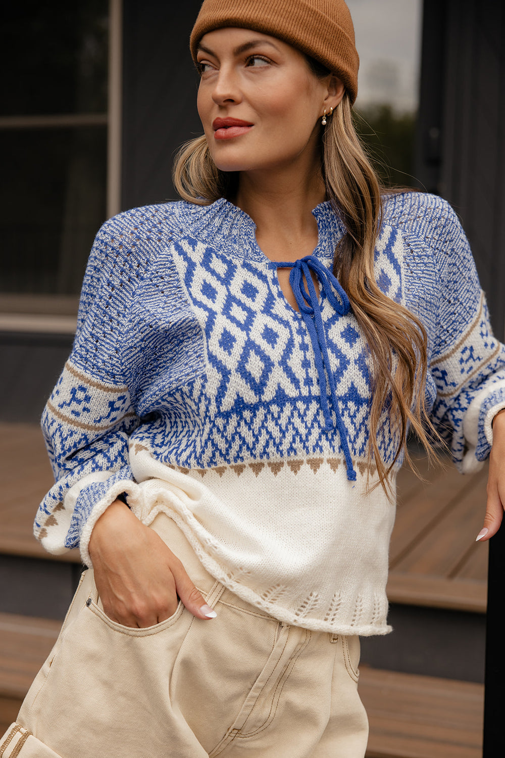 Woman wearing a blue and white patterned sweater with beige pants and a brown beanie.