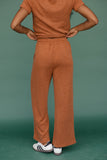 Person wearing a brown outfit with wide-leg pants against a green background
