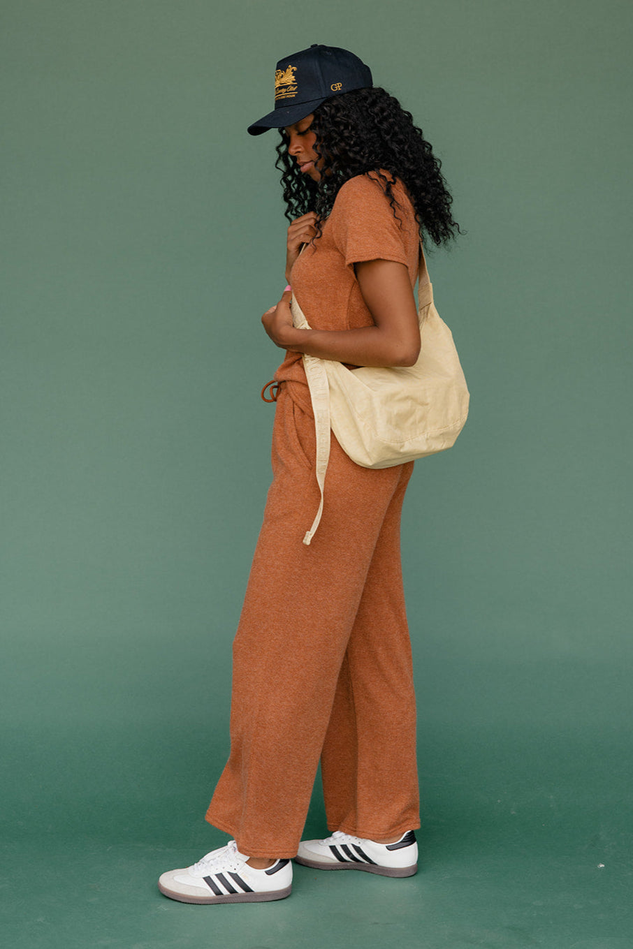 Woman in a brown outfit with a beige bag against a green background