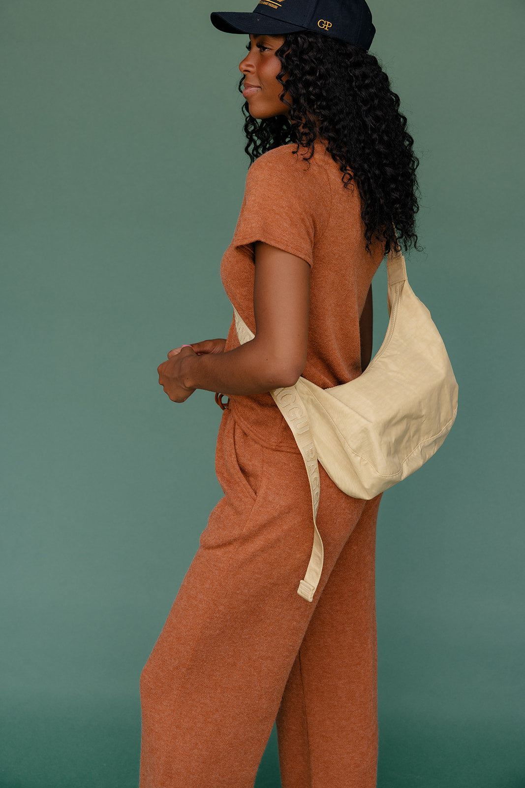 Woman in a rust-colored outfit with a beige bag against a teal background