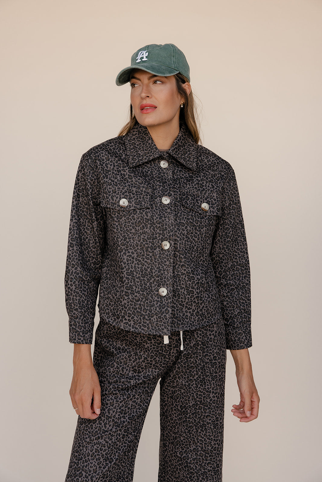 Woman wearing a black patterned outfit with a cap on a beige background