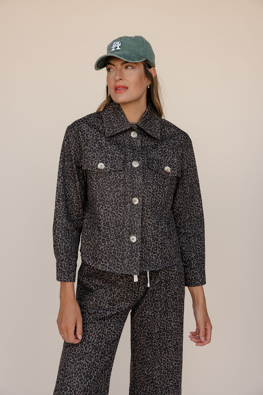 Woman wearing a black patterned outfit with a cap on a beige background