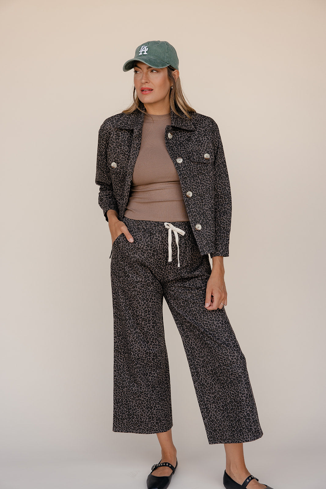 Woman wearing a patterned jacket and pants with a cap on a beige background