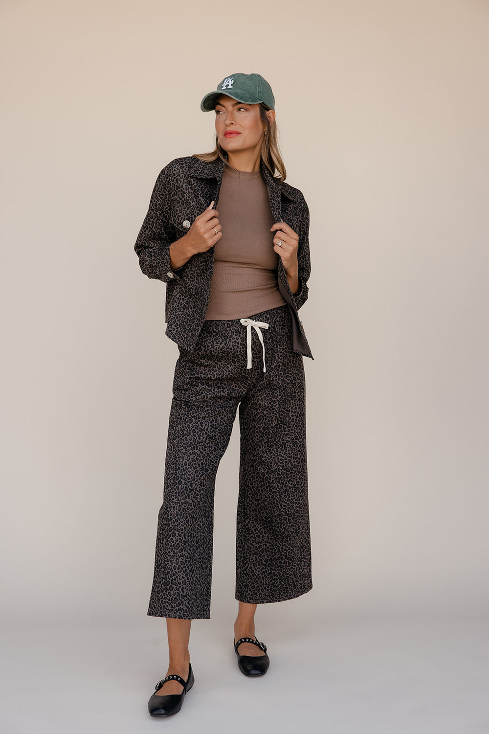 Woman wearing a patterned jacket and pants with a cap on a beige background