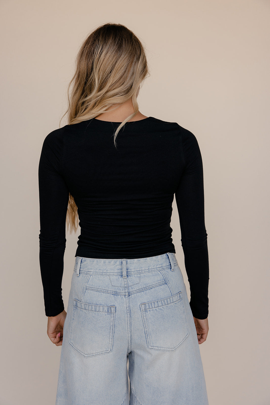 Person wearing a black long-sleeve top and light blue jeans against a beige background