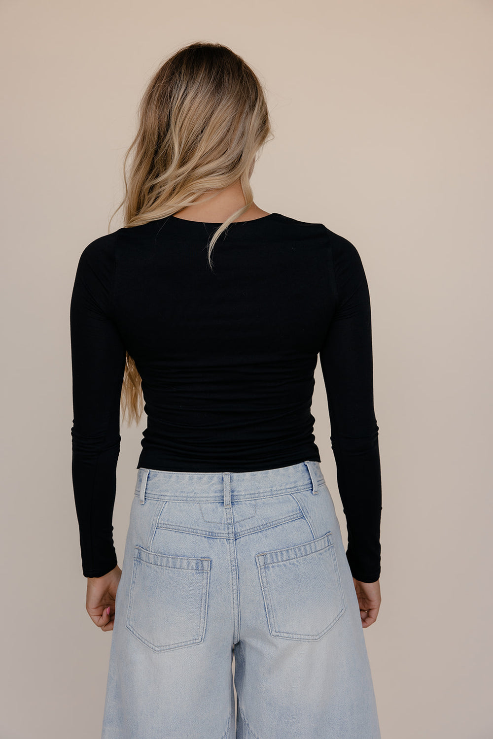 Person wearing a black long-sleeve top and light blue jeans against a beige background