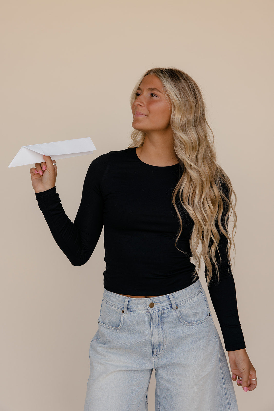 Woman holding a white paper airplane against a beige background