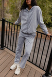 Person wearing a gray tracksuit standing on a wooden deck with greenery in the background