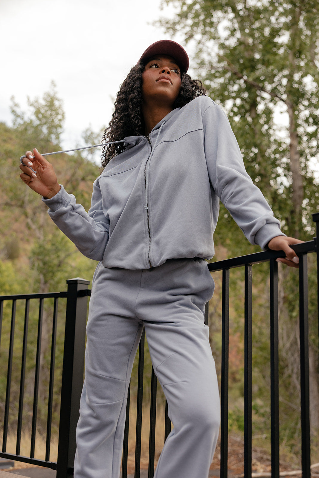 Woman in a gray tracksuit standing outdoors with trees in the background