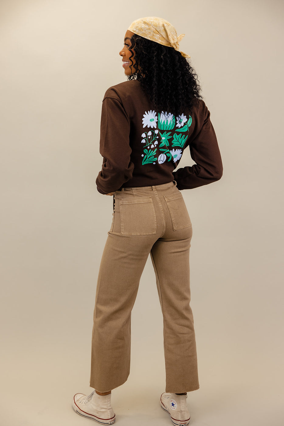 a woman wearing brown pants and brown sweater with a floral design on the back
