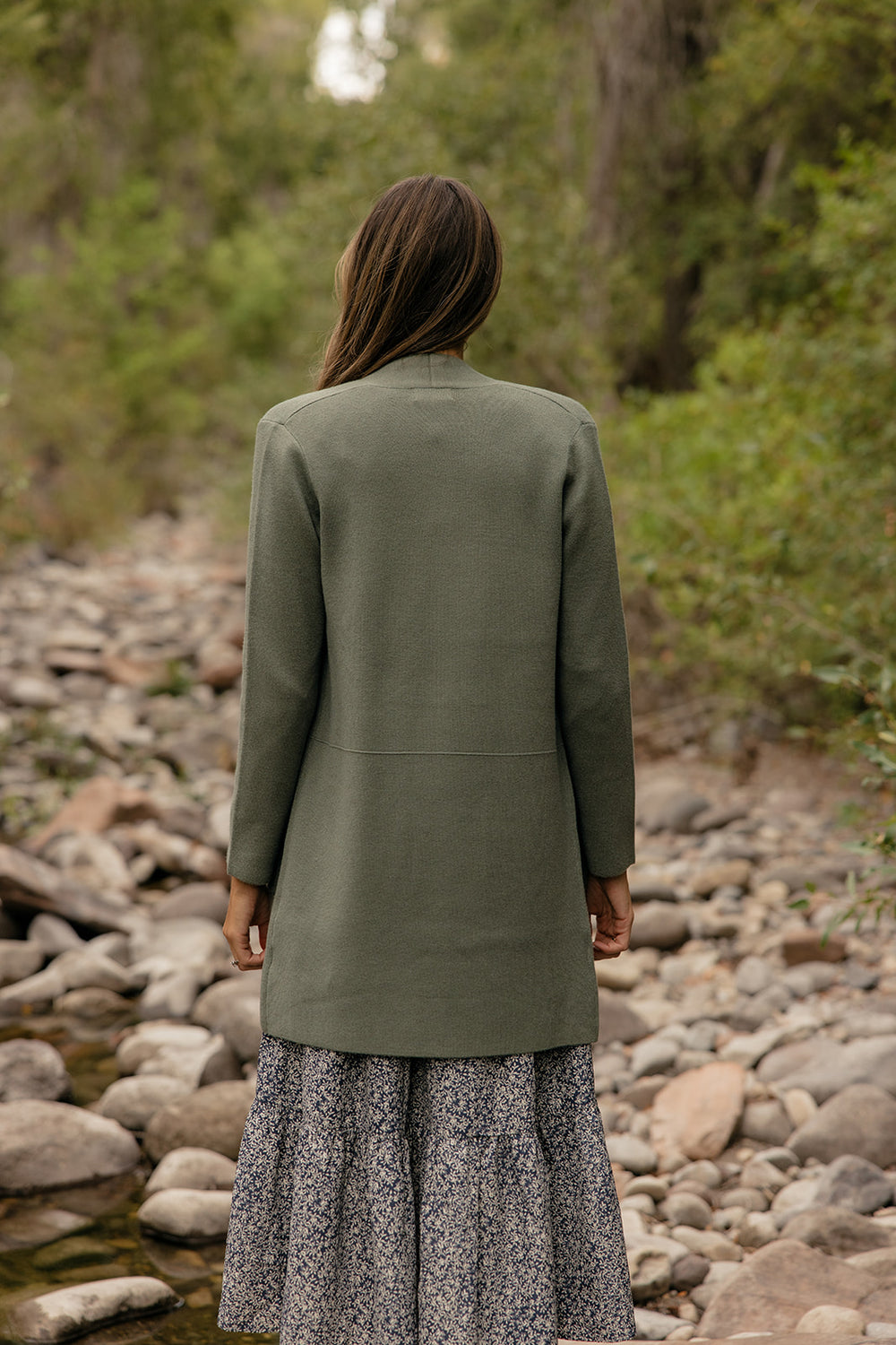 Person wearing a green jacket standing by a stream with a natural background
