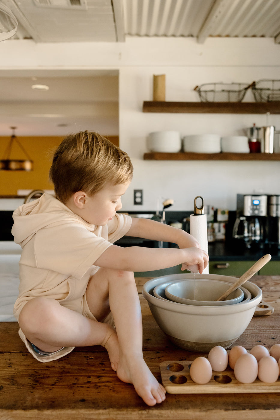 a boy sitting on a counter with a bowl of eggs and a wooden spoon