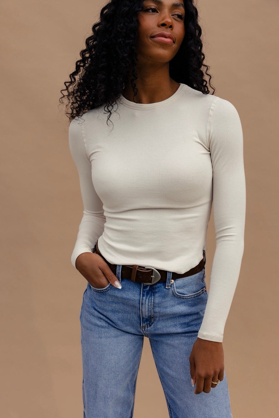 a woman with long curly hair wearing a white shirt and blue jeans