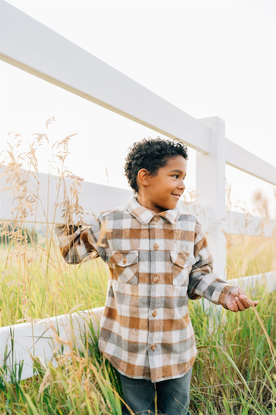 a boy standing in tall grass next to a white fence