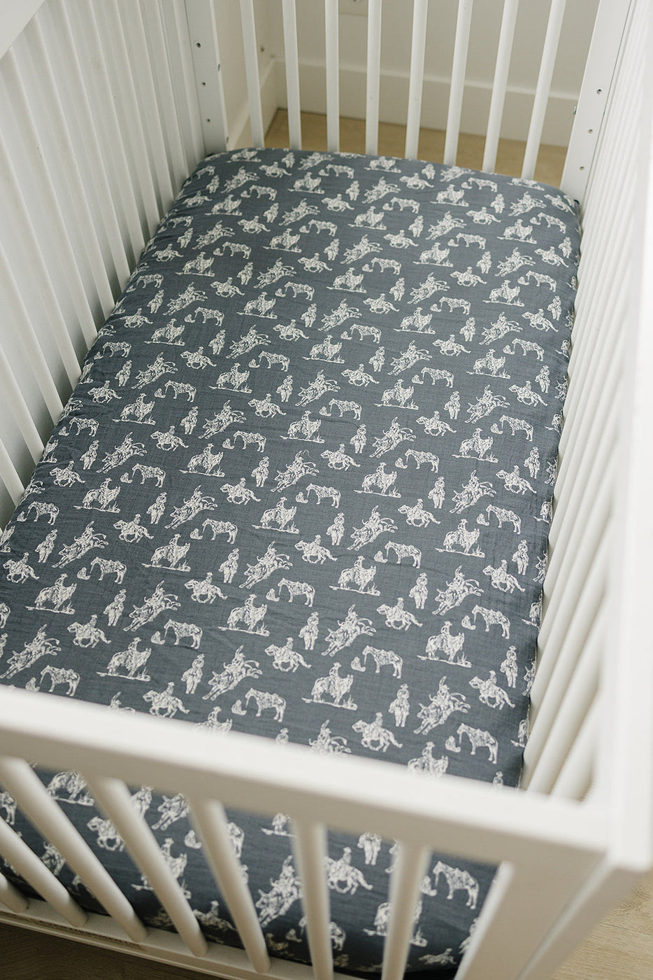 a crib with a black and white sheet with horses on it