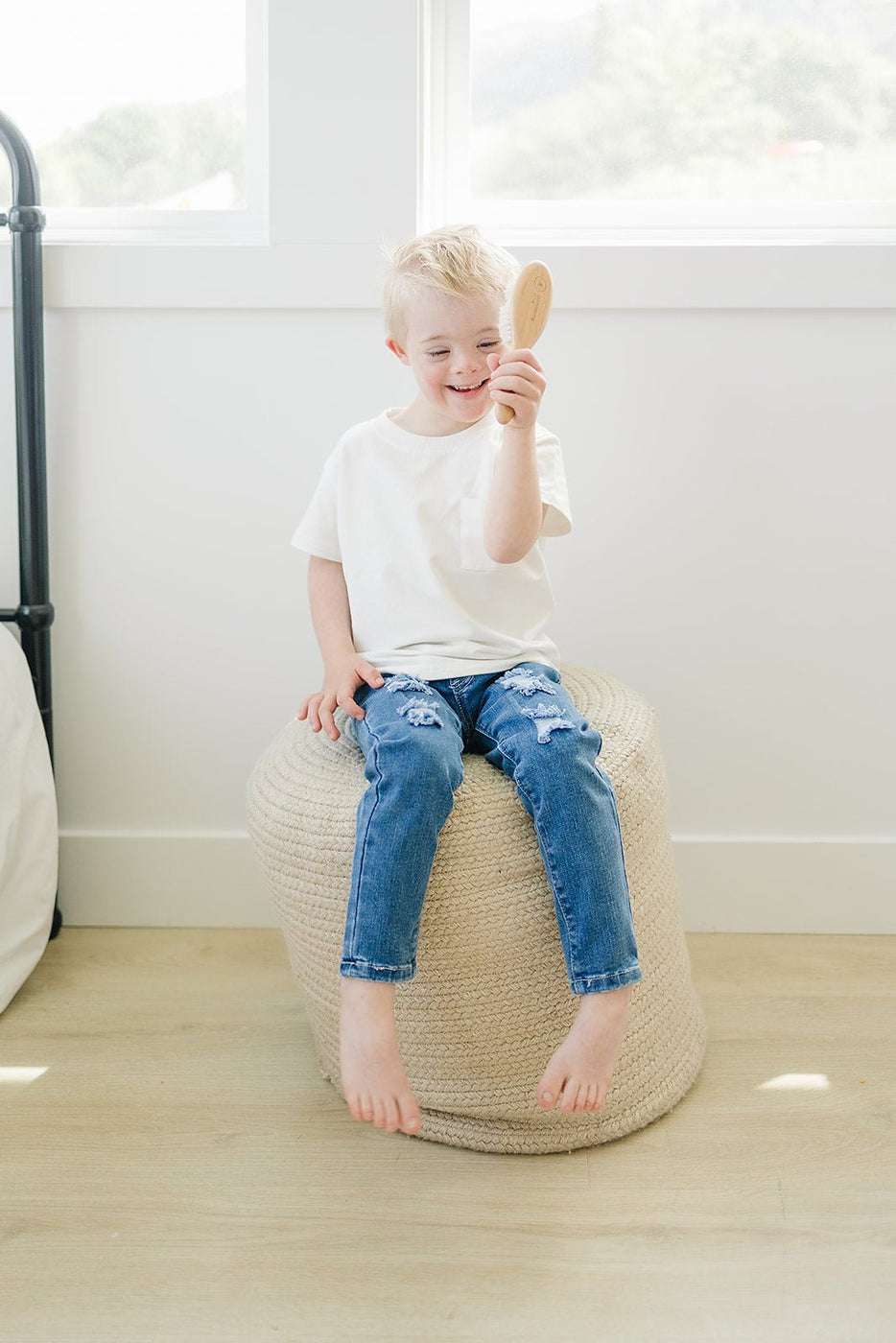 a boy sitting on a stool holding a hair brush