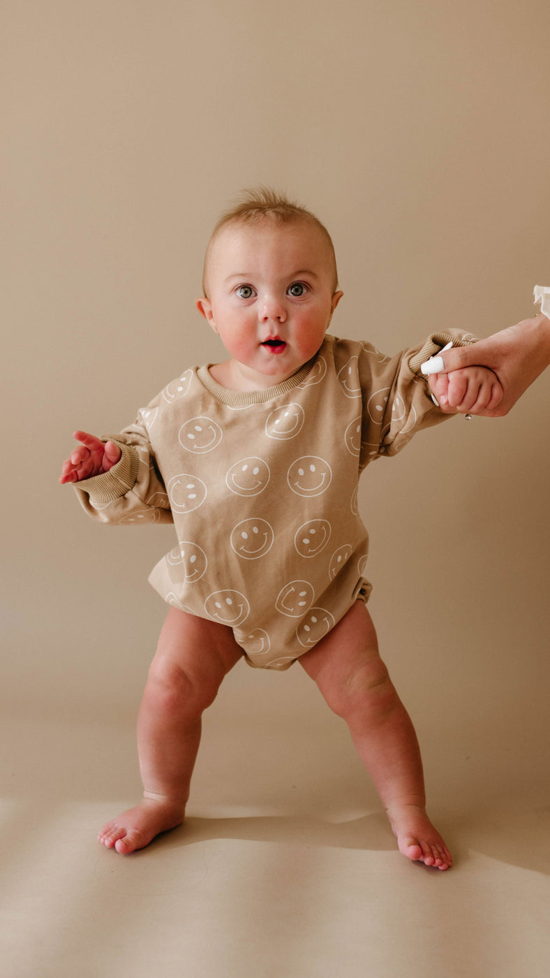 a baby standing in front of a beige wall