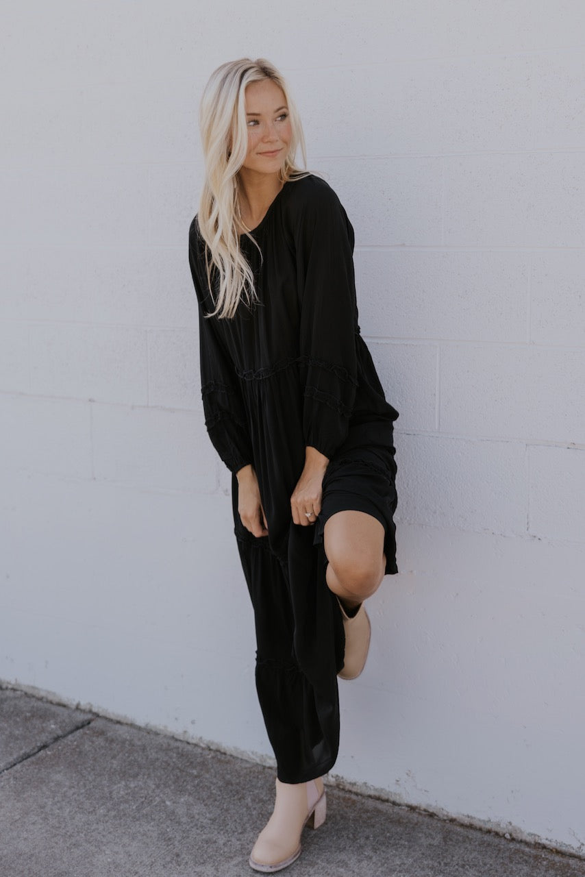 a woman in a black dress leaning against a wall